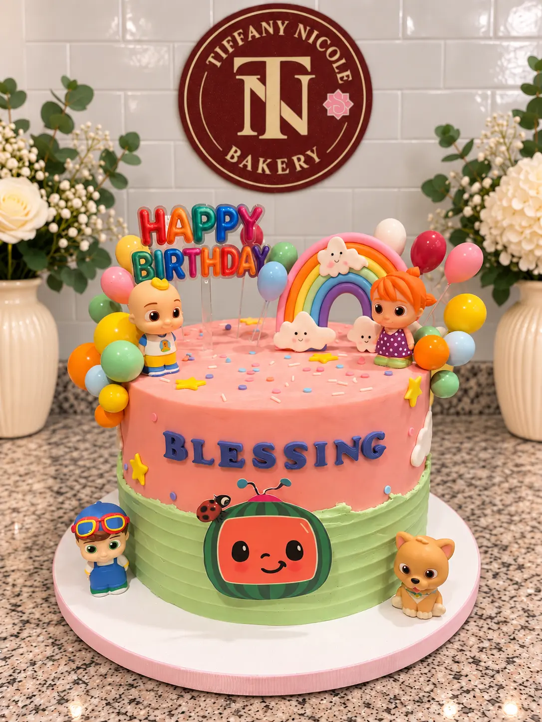 Pink and green CoComelon themed birthday cake with rainbow arch, balloons and Blessing lettering