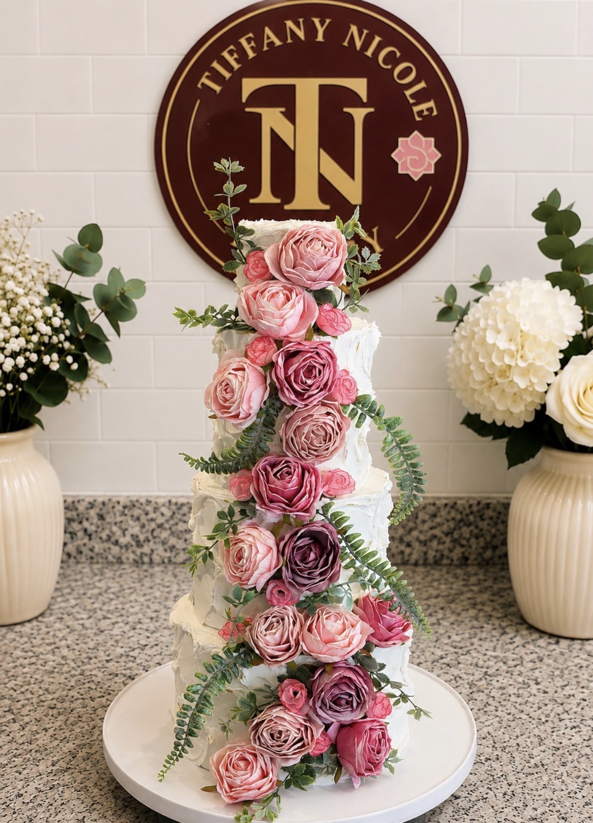 Tall white wedding cake with a cascade of pink and burgundy roses